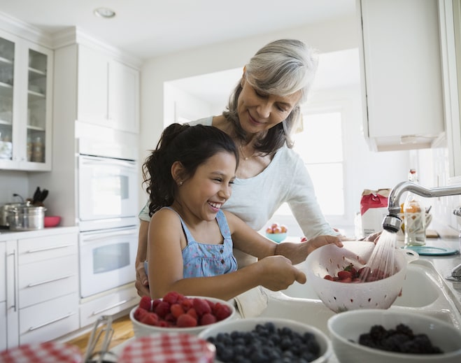 Child washing berries with older adult