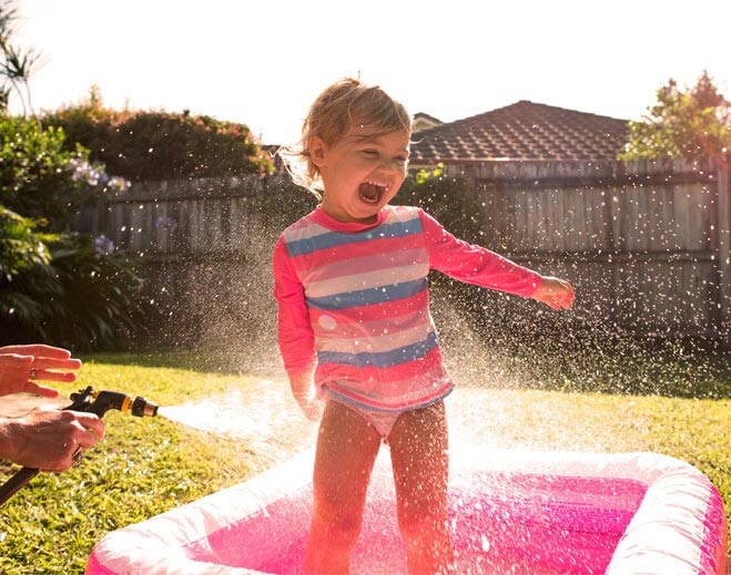 Child playing outdoors with water spray